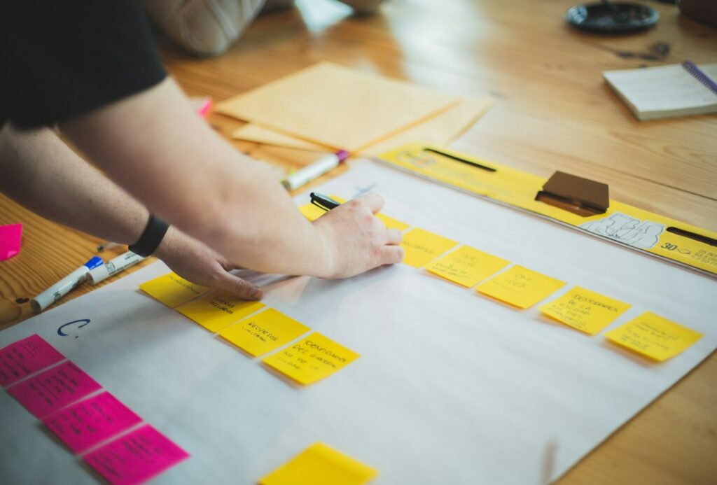 Hands arranging notes into a practical project plan on a desk.