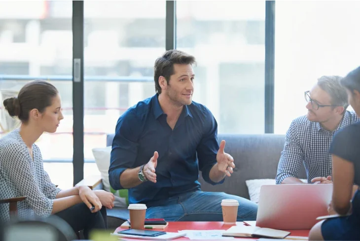 People exchanging ideas around a table in a comfortable meeting area.