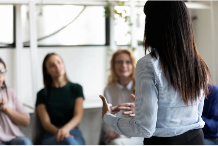 A facilitator speaking with a small group of seated attendees.